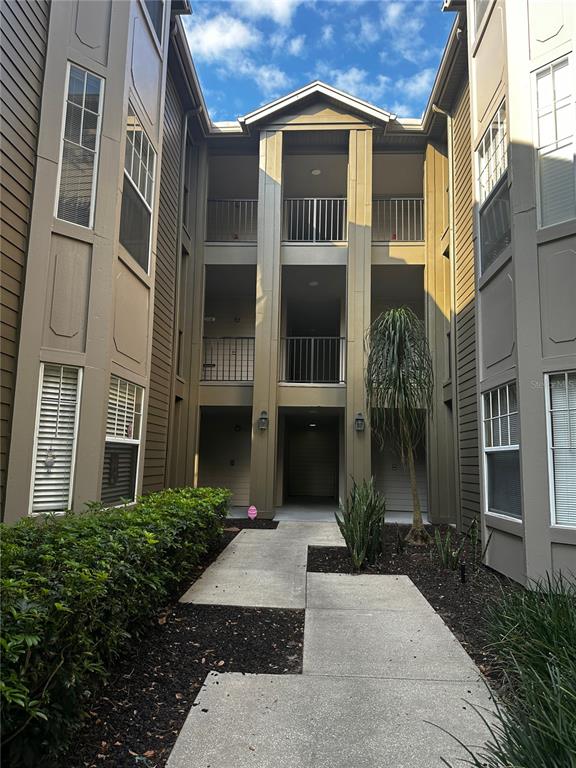 A concrete walkway leads to the entrance of a three-story apartment building with tan siding — 420 SUMMIT RIDGE PLACE UNIT 204, LONGWOOD, FL