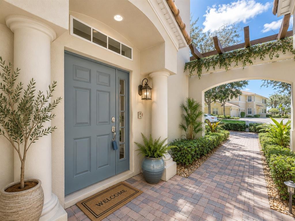 A blue front door with a side window sits under an arched entryway with columns — 1338 EMERALD DUNES DRIVE UNIT 35, SUN CITY CENTER, FL