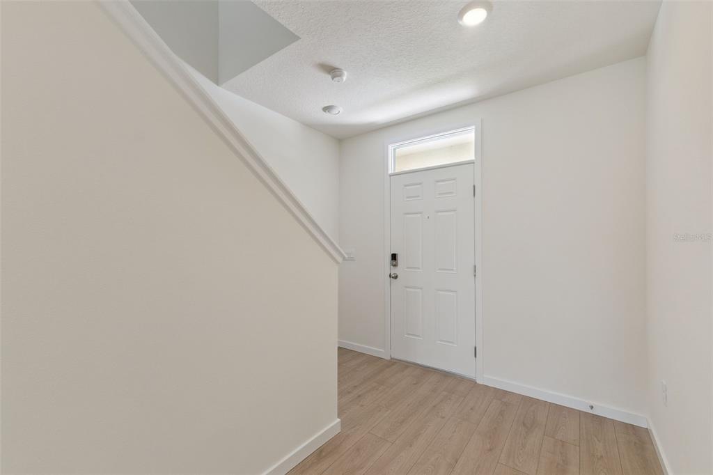 An entryway features light wood-look flooring, a white front door, and a staircase — 1344 GRAND FLORA LANE, SANFORD, FL