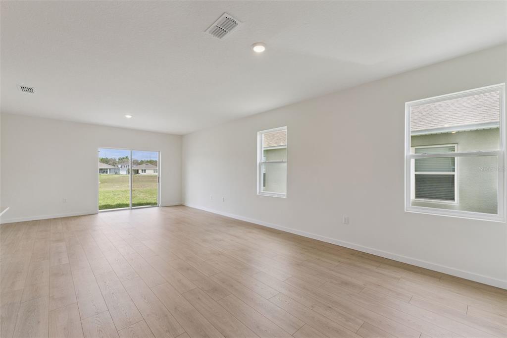 An empty room with light wood-look flooring, white walls, a sliding glass door, and windows — 1344 GRAND FLORA LANE, SANFORD, FL