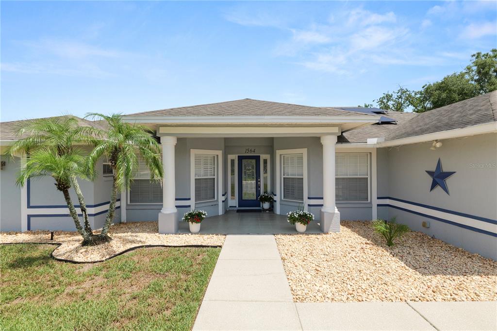 A gray single-story house features a covered entryway with white columns and a blue star — 1564 NORWICK WAY, LAKELAND, FL