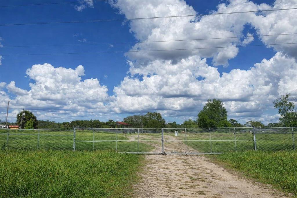 A gated chain-link fence surrounds a grassy, vacant lot under a bright blue sky — MARICAMP RD, OCALA, FL