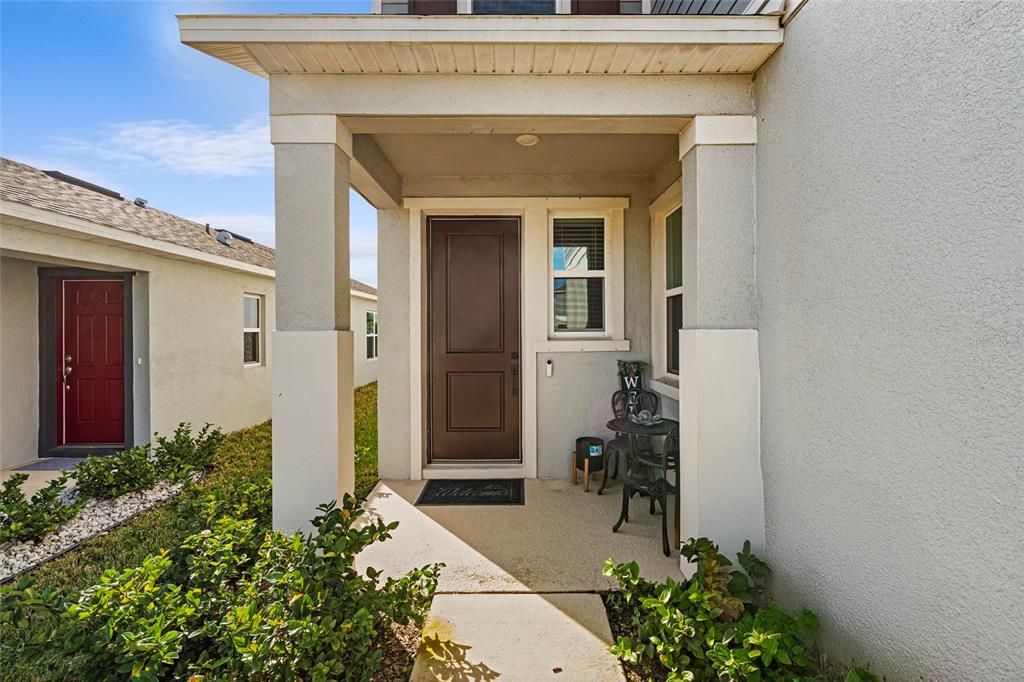 A covered front porch features a brown door, a small bistro set, and landscaping — 2854 89TH STREET CIRCLE E, PALMETTO, FL