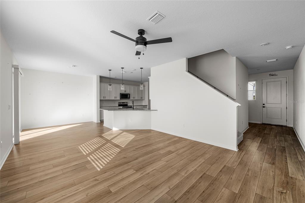An open-concept living area features light wood-look flooring, a kitchen with white cabinets, and stairs — 2854 89TH STREET CIRCLE E, PALMETTO, FL