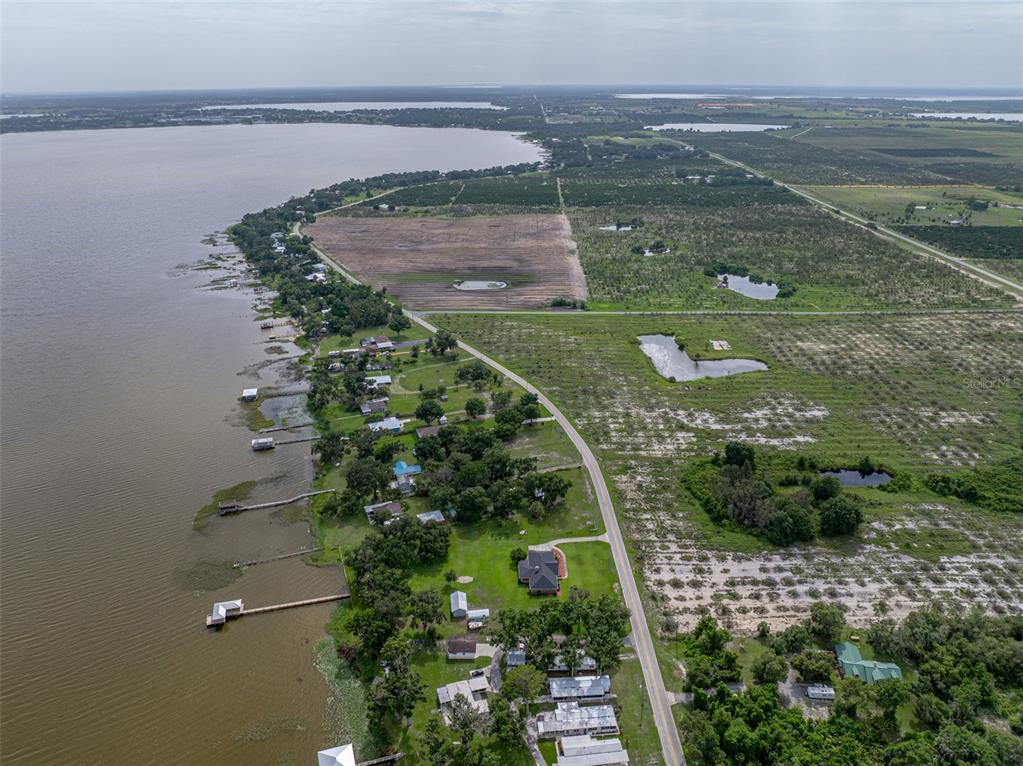 An aerial view shows houses along a lakeshore next to fields and a paved road — 0 LAKE REEDY BOULEVARD, FROSTPROOF, FL