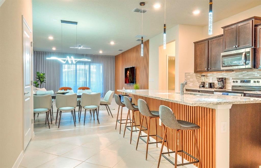 A modern kitchen with a slatted wood island and bar stools overlooks an open dining area — 16231 TRINIDAD WAY, CLERMONT, FL