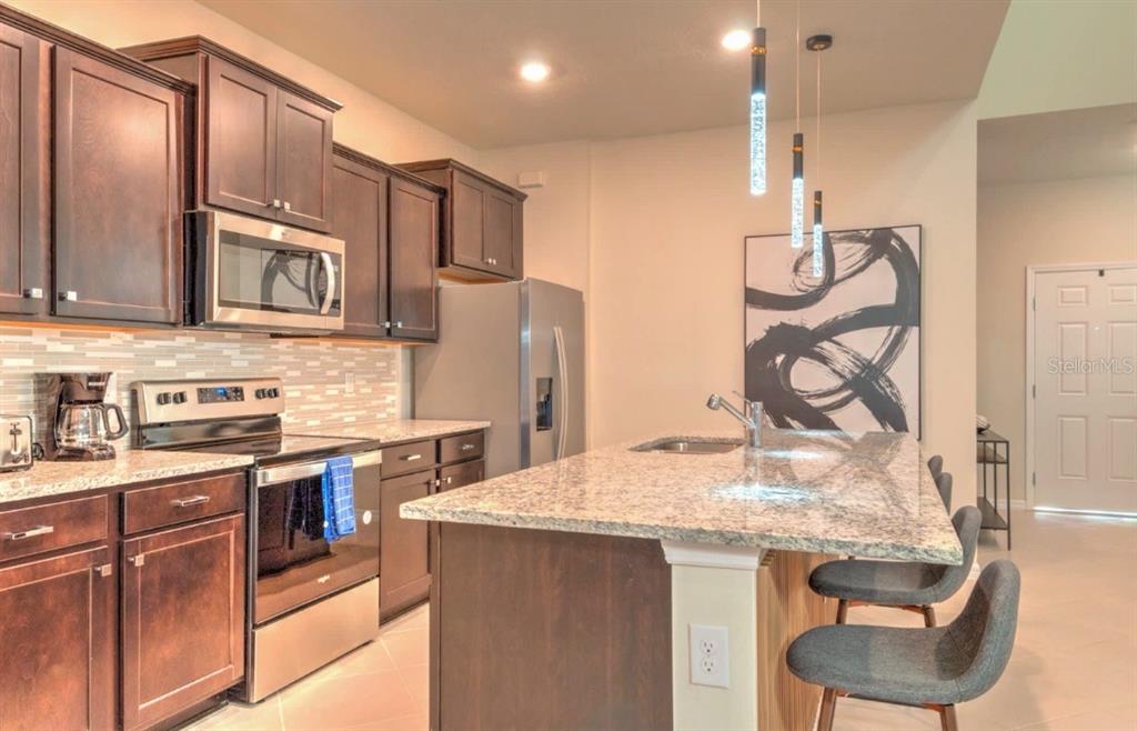 A kitchen features dark wood cabinets, granite countertops, a stainless steel island, and pendant lighting — 16231 TRINIDAD WAY, CLERMONT, FL