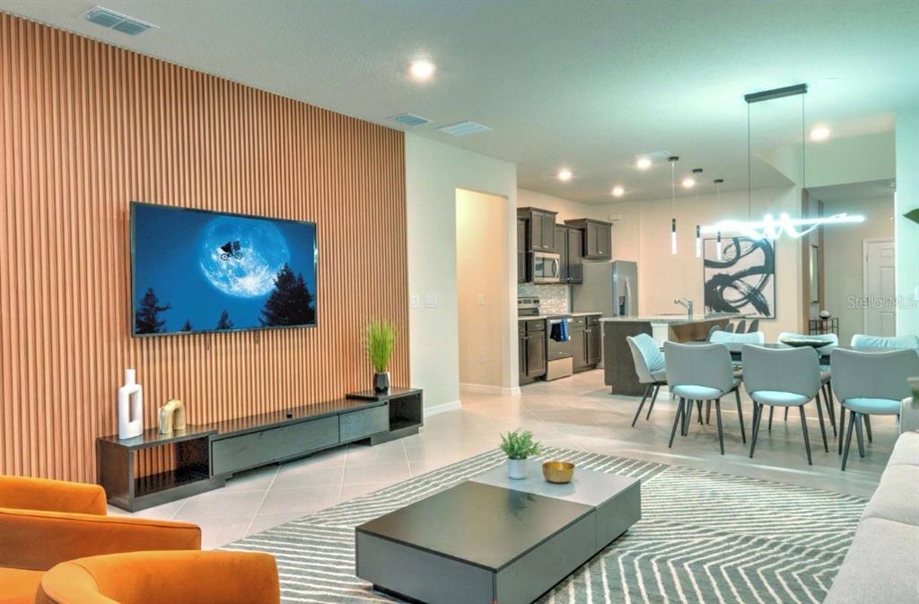 A living room with a slatted wood accent wall, television, and adjacent open-concept kitchen — 16231 TRINIDAD WAY, CLERMONT, FL