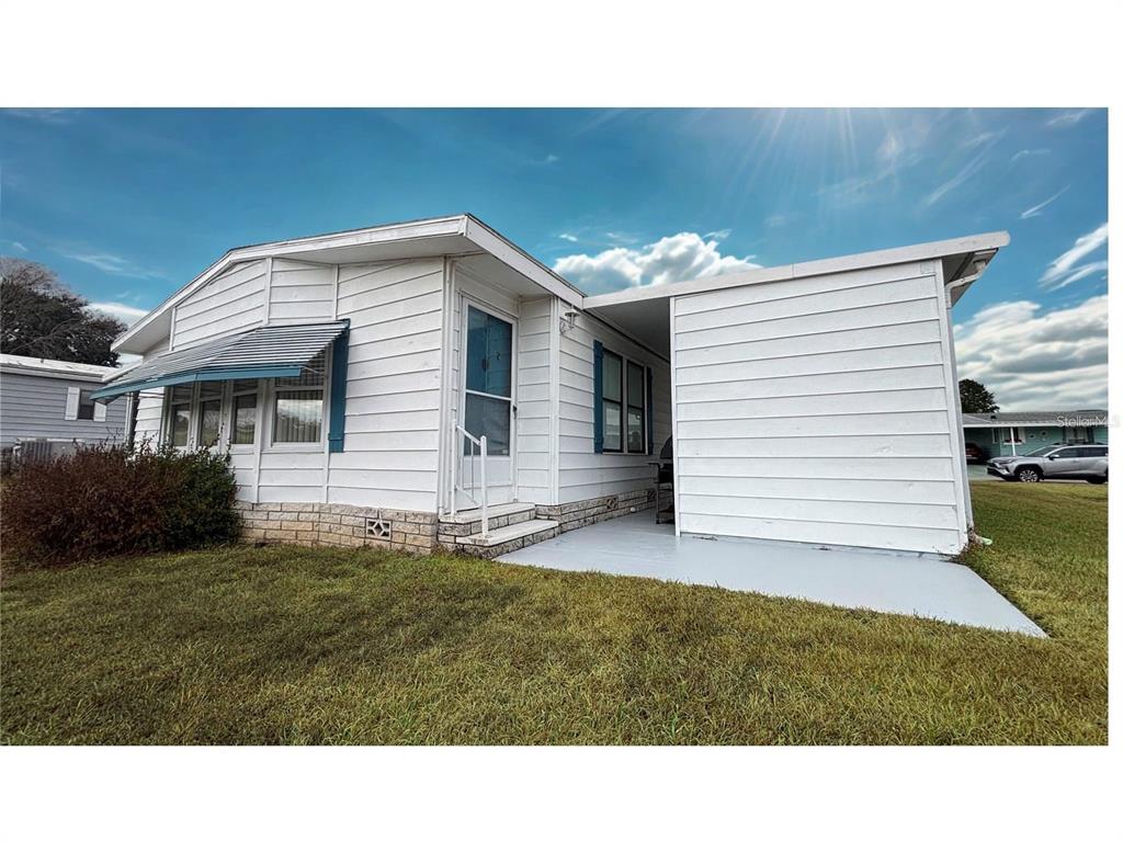A white mobile home features a covered patio, horizontal siding, and a small brick foundation — 3746 PARWAY ROAD UNIT 1349, ZELLWOOD, FL