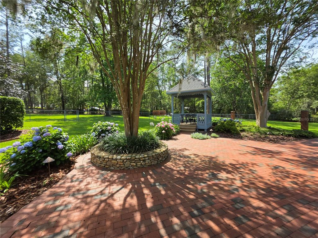 A brick patio features a stone-bordered tree planter and a blue gazebo in a backyard — 4326 SW 80TH STREET, GAINESVILLE, FL