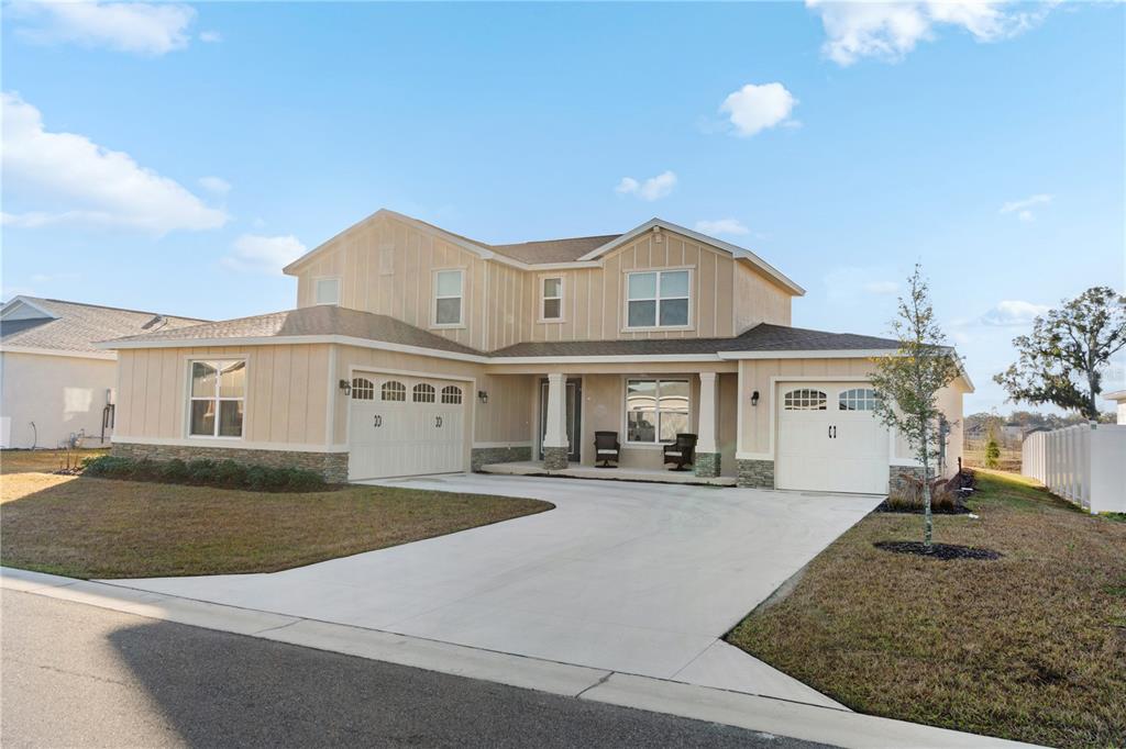 A two-story house with tan vertical siding, stone accents, and a three-car garage — 7610 SW 60TH STREET, OCALA, FL