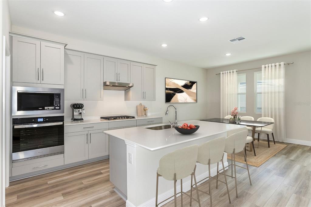 A modern kitchen features light gray cabinetry, a central island with seating, and stainless appliances — 33531 HAMMOCK BEACH WAY, DADE CITY, FL