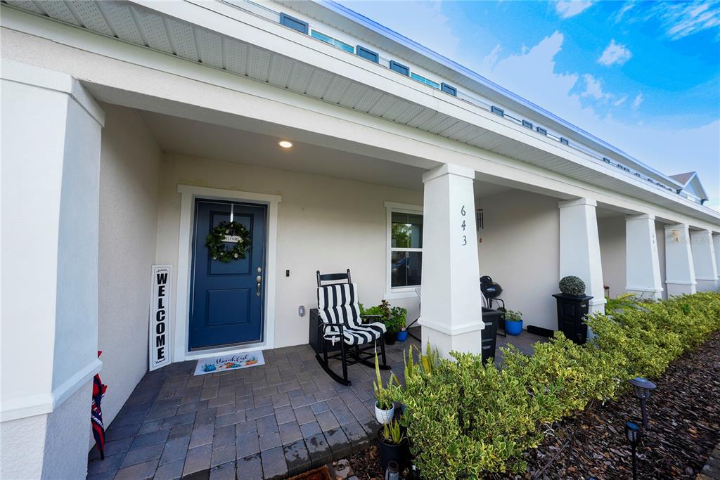 A covered front porch features a blue door, a rocking chair, and a paved floor — 643 BELGROVE STREET, DEBARY, FL