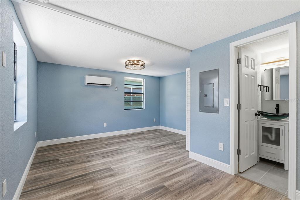 A blue-walled room with wood-look flooring, a mini-split AC unit, and an attached bathroom — 113 145TH AVENUE E UNIT 3, MADEIRA BEACH, FL