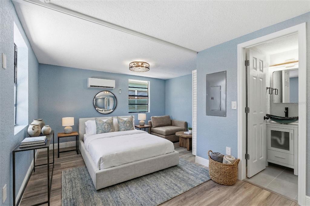 A bedroom with light blue walls, a bed, a small armchair, and an attached bathroom — 113 145TH AVENUE E UNIT 3, MADEIRA BEACH, FL