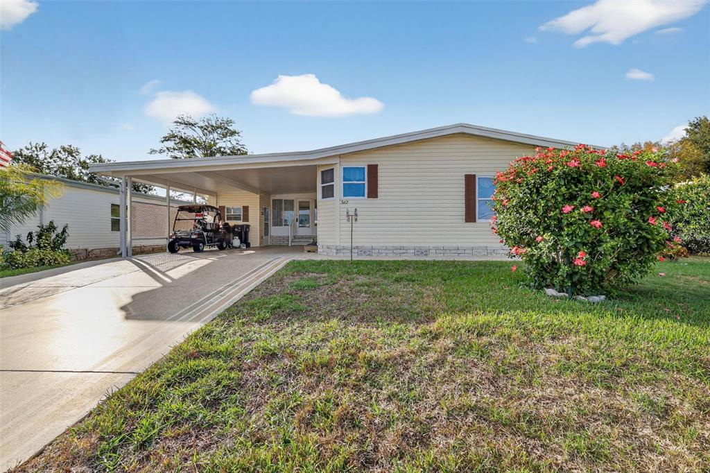 A single-story manufactured home with a carport, concrete driveway, and a large flowering bush — 3117 MANATEE ROAD, TAVARES, FL