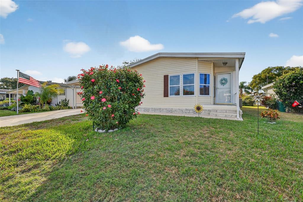 A single-story manufactured home with light siding, a front porch, and a large flowering bush — 3117 MANATEE ROAD, TAVARES, FL