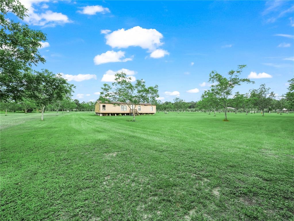 A tan manufactured home sits in the middle of a large, grassy, tree-filled field — 8564 CAREY ROAD, LITHIA, FL