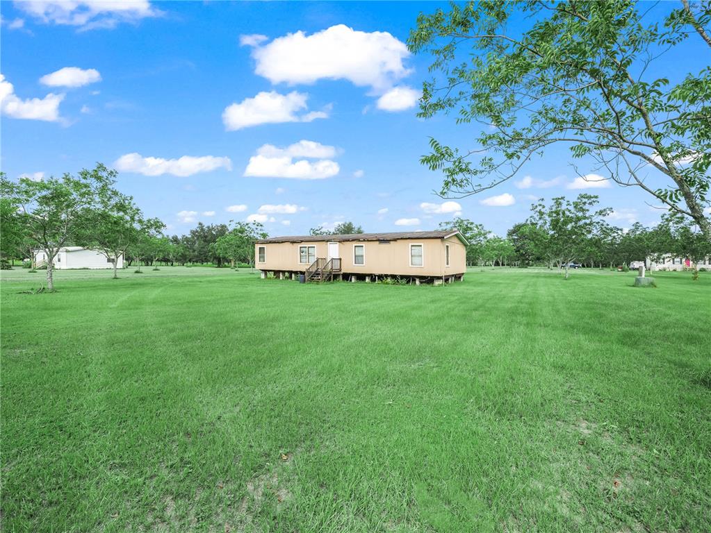 A tan mobile home sits in the middle of a large, grassy field under blue skies — 8564 CAREY ROAD, LITHIA, FL