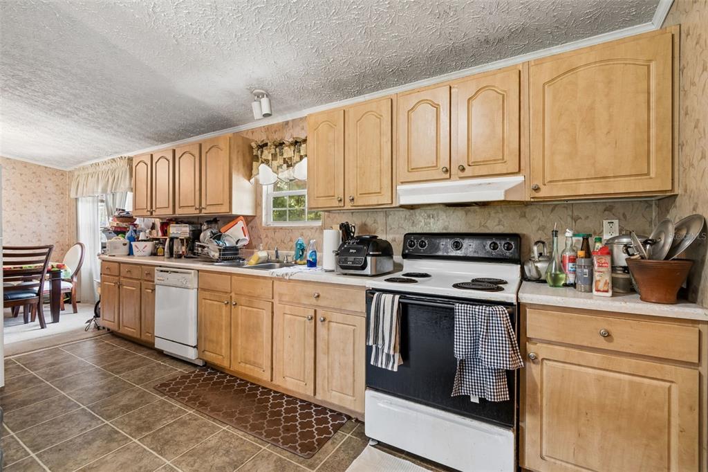 A kitchen features light wood cabinets, a white stove, a dishwasher, and patterned wallpaper — 11101 SUMNER ROAD, WIMAUMA, FL