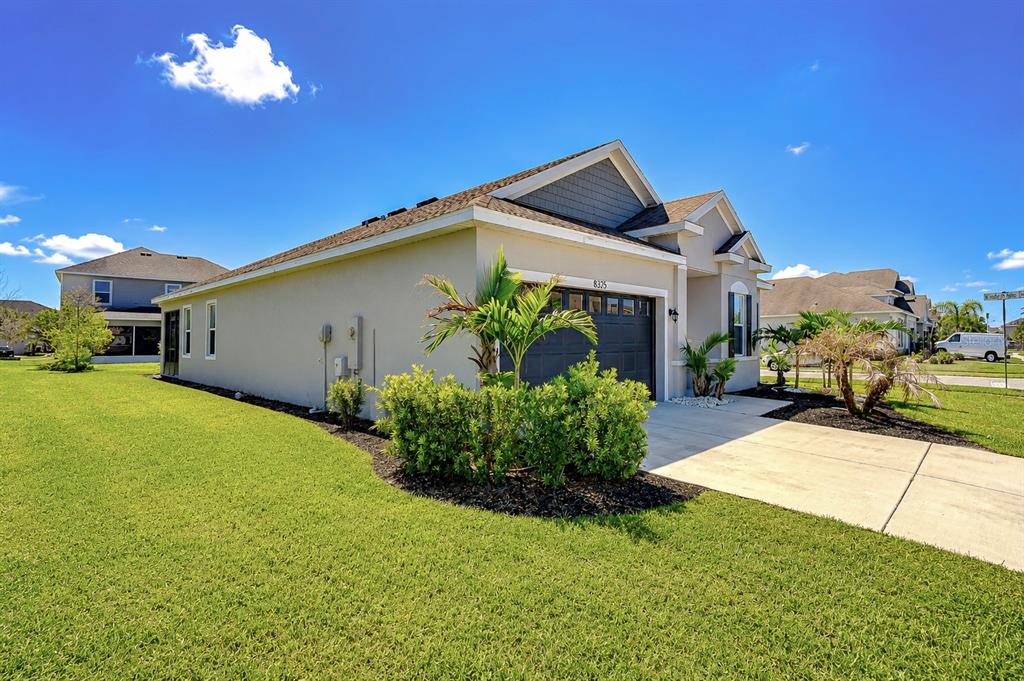 A single-story house with a two-car garage, tan stucco siding, and a landscaped front yard — 8325 OLIVE BROOK DRIVE, WESLEY CHAPEL, FL