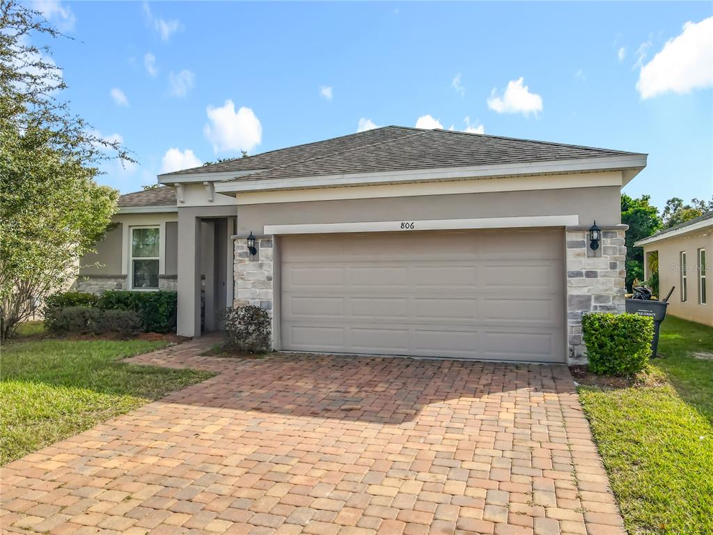 A single-story house with a beige stucco exterior, stone accents, and a brick paver driveway — 806 BENJAMIN TRAIL, DAVENPORT, FL