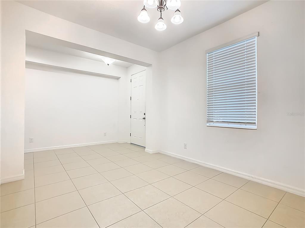 A bright, empty room features white walls, light-colored tile flooring, a window with blinds, and a chandelier — 806 BENJAMIN TRAIL, DAVENPORT, FL