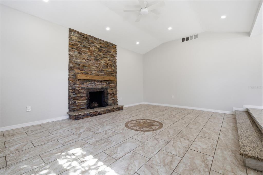 A living room features a stone fireplace, tile flooring, and a vaulted ceiling with lighting — 1201 S LINCOLN AVENUE, LAKELAND, FL