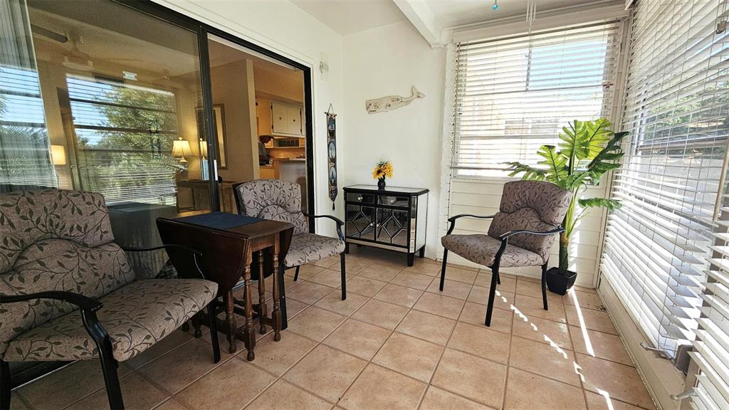 A sunroom with tile flooring, three patterned armchairs, a wooden side table, and window blinds — 3586 CAPEHAZE DRIVE UNIT B4, ROTONDA WEST, FL