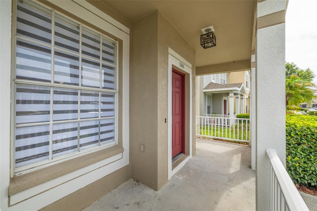 A covered entryway features a red front door, a large window, and a white railing — 3441 RED ROCK DRIVE, LAND O LAKES, FL