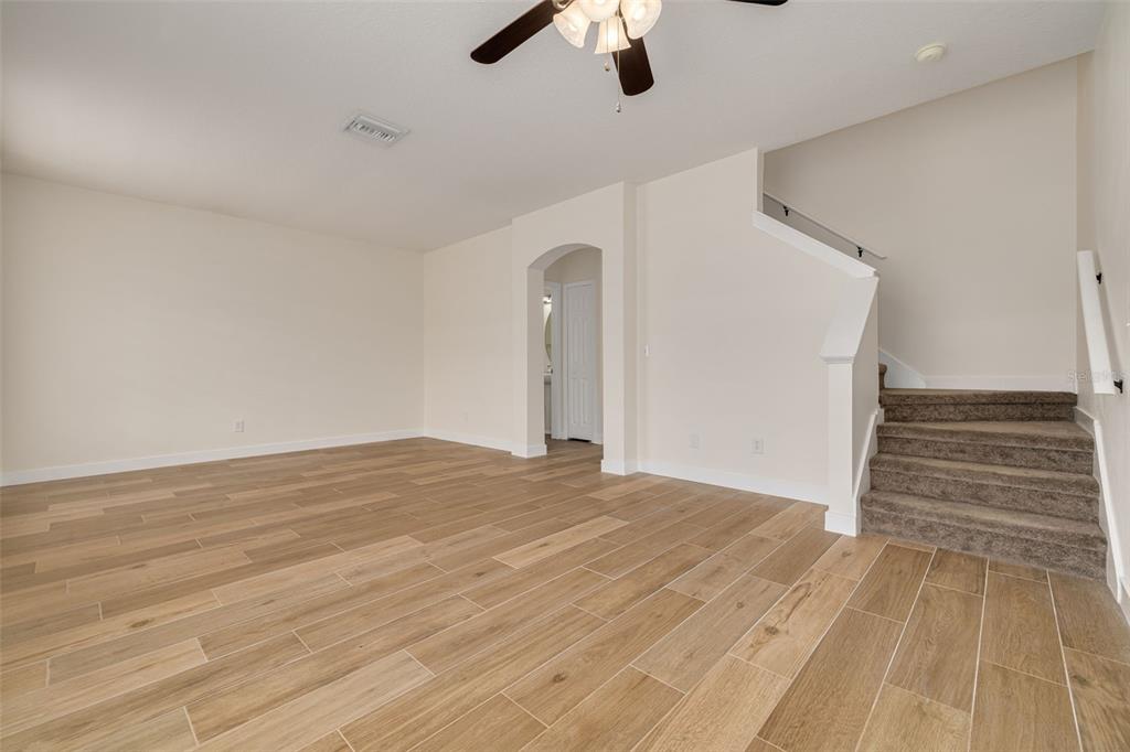 An empty room features light wood-look tile flooring, beige walls, and carpeted stairs — 3441 RED ROCK DRIVE, LAND O LAKES, FL