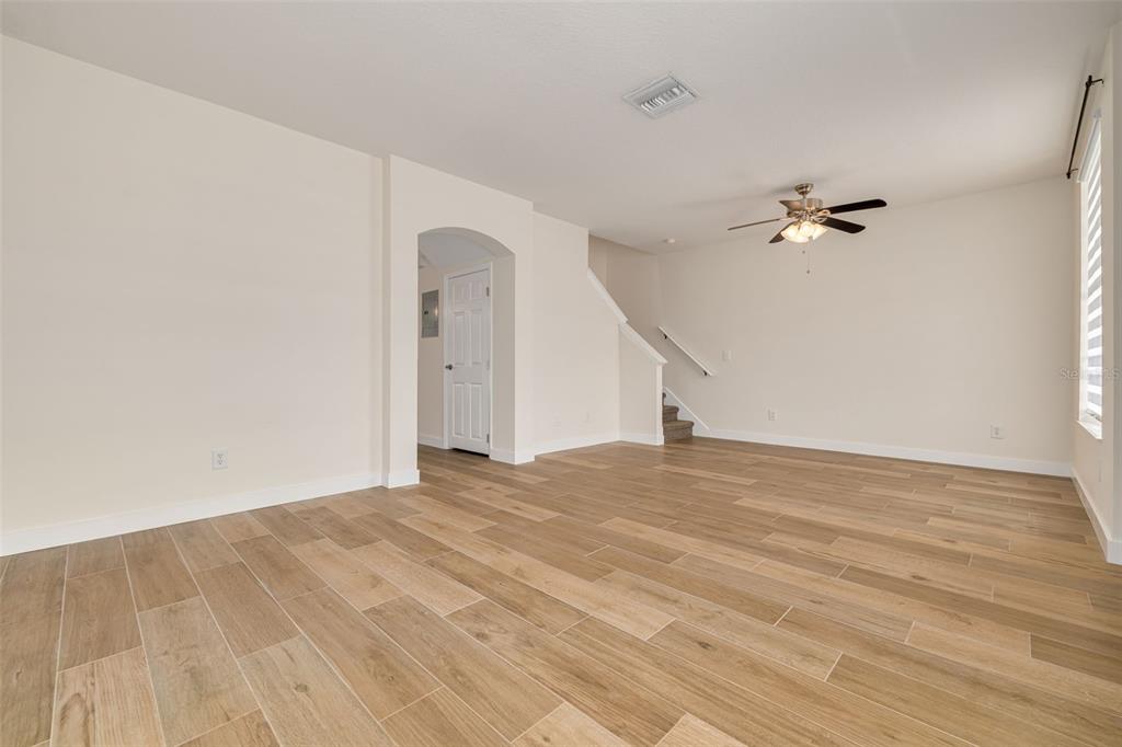 An empty living room features light wood-look tile flooring, white walls, and a ceiling fan — 3441 RED ROCK DRIVE, LAND O LAKES, FL