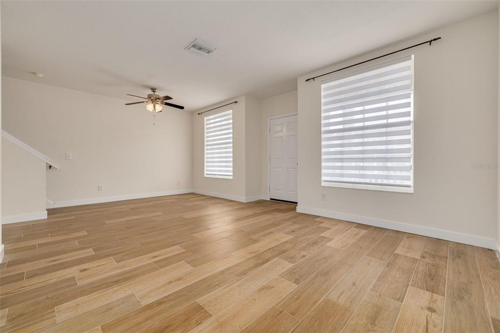 An empty living room features light wood-look tile flooring, white walls, and two windows — 3441 RED ROCK DRIVE, LAND O LAKES, FL