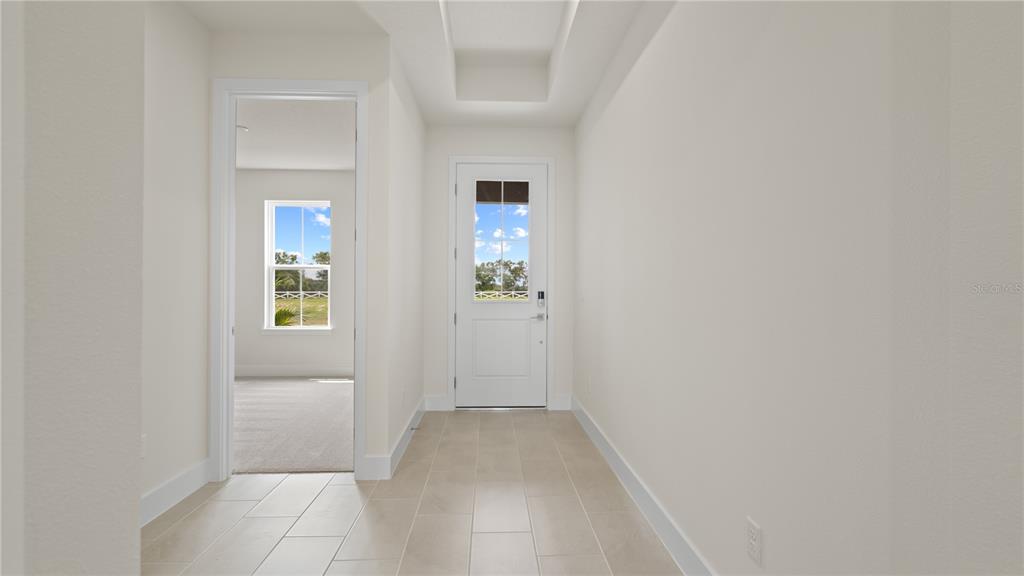 A bright entryway with light tile flooring leads to a white door and a bedroom — 30273 RUSTIC MILL STREET, MOUNT DORA, FL