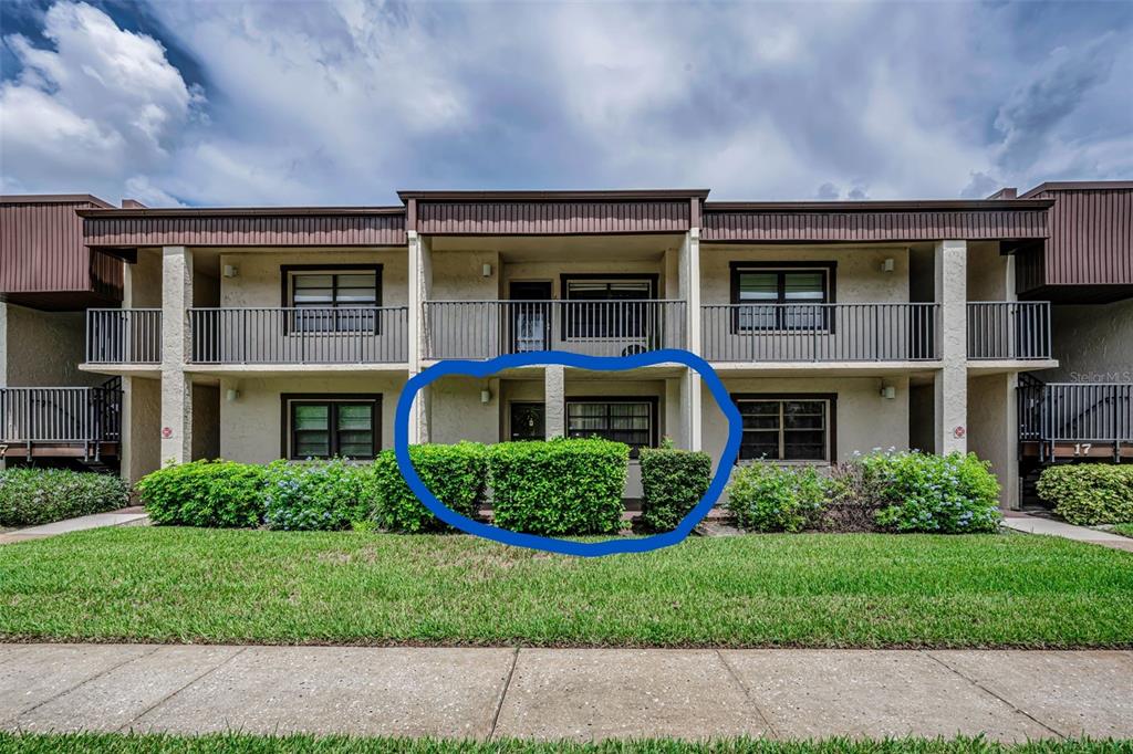 The exterior of a two-story apartment building features a ground-floor unit with a privacy hedge — 2400 WINDING CREEK BOULEVARD UNIT 17-103, CLEARWATER, FL