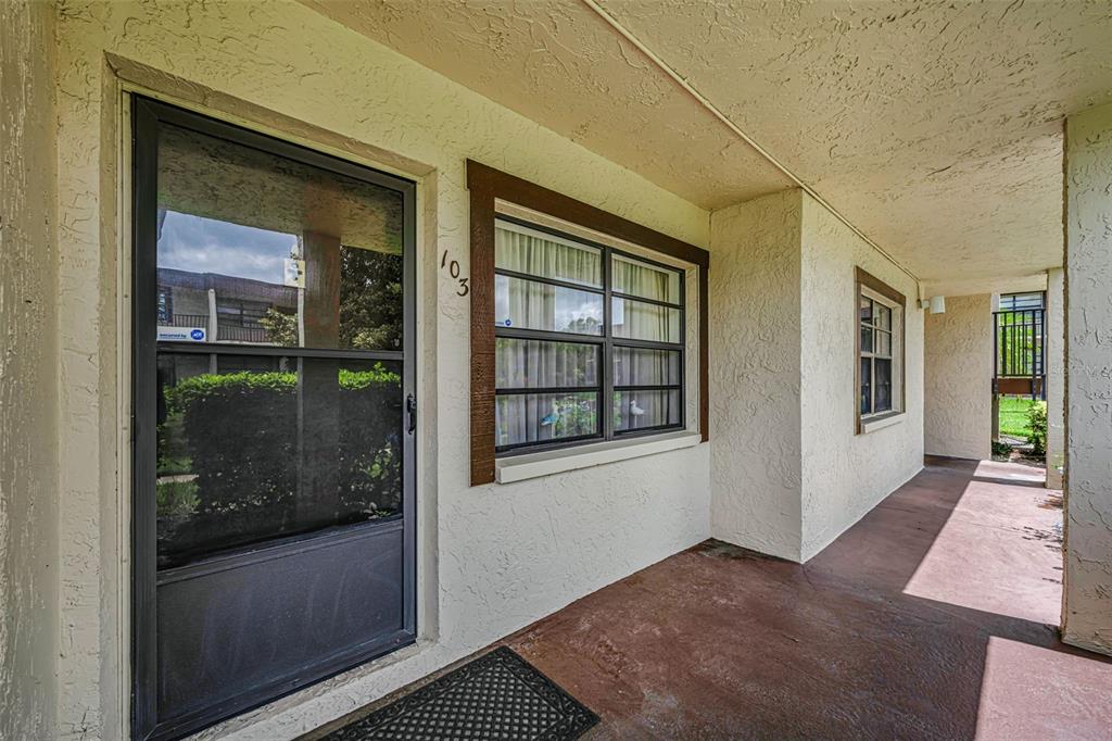 A covered exterior walkway leads to a front door and window labeled with the number 103 — 2400 WINDING CREEK BOULEVARD UNIT 17-103, CLEARWATER, FL