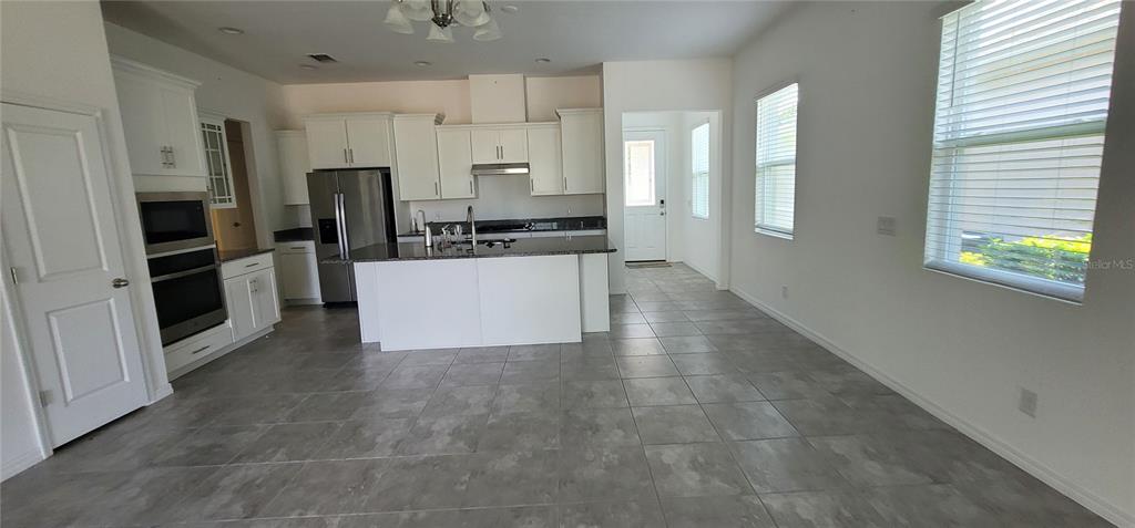 A kitchen features white cabinetry, a central island, stainless steel appliances, and gray tile flooring — 1908 FLORA PASS PLACE, KISSIMMEE, FL