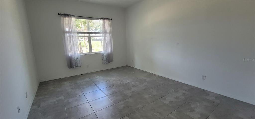 An empty room with white walls, large gray floor tiles, and a window with curtains — 1908 FLORA PASS PLACE, KISSIMMEE, FL