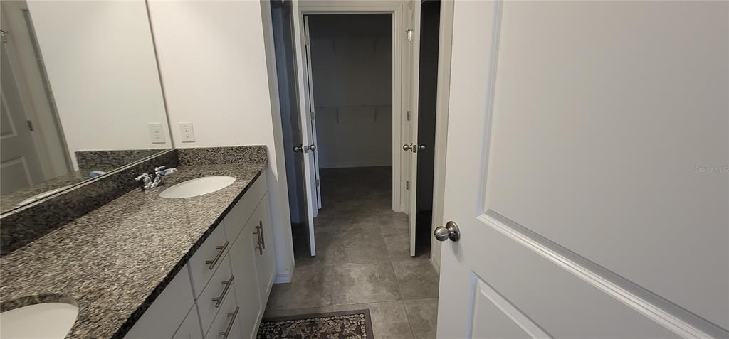 A bathroom features a granite-topped vanity with double sinks and an adjacent walk-in closet — 1908 FLORA PASS PLACE, KISSIMMEE, FL