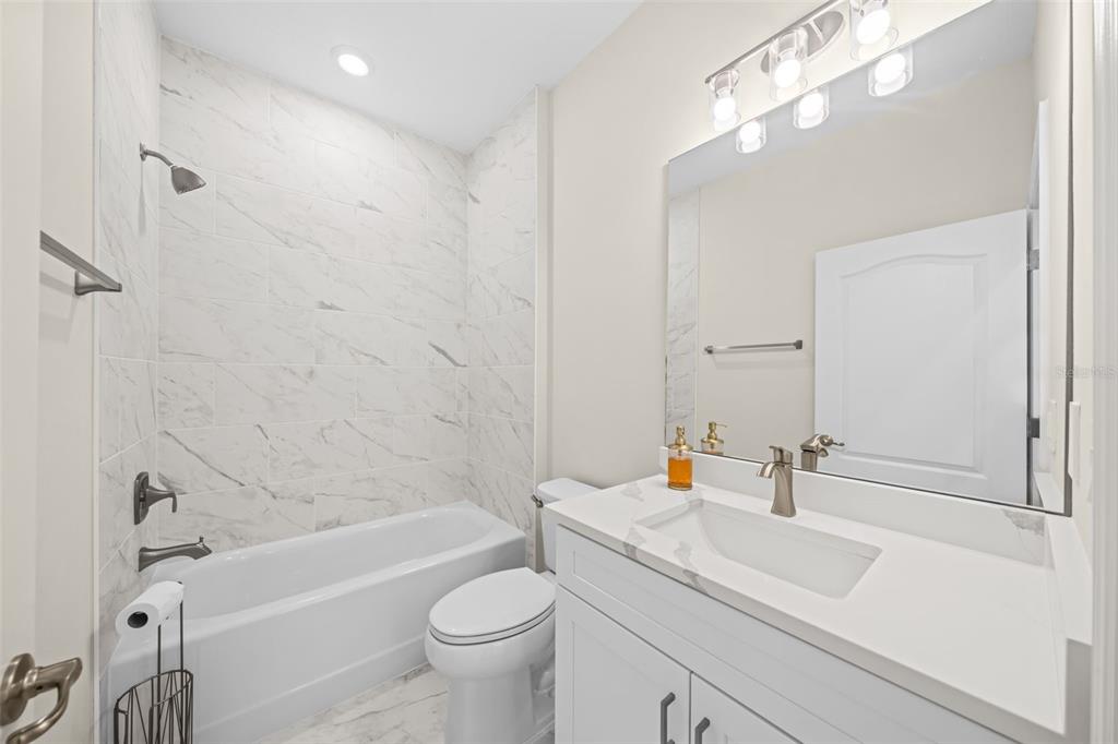 A bathroom with a white vanity, a toilet, and a bathtub with marble-look tile walls — 3181 LA FRANCE AVENUE SW, PALM BAY, FL