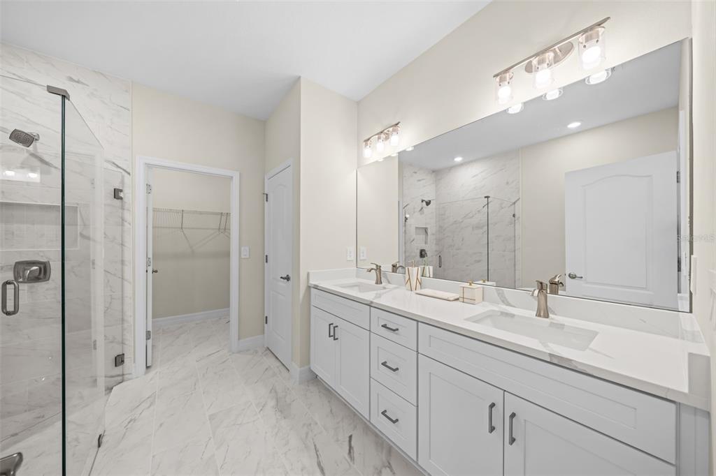 A modern bathroom features a double vanity with white cabinets, marble-look flooring, and a glass shower — 3181 LA FRANCE AVENUE SW, PALM BAY, FL