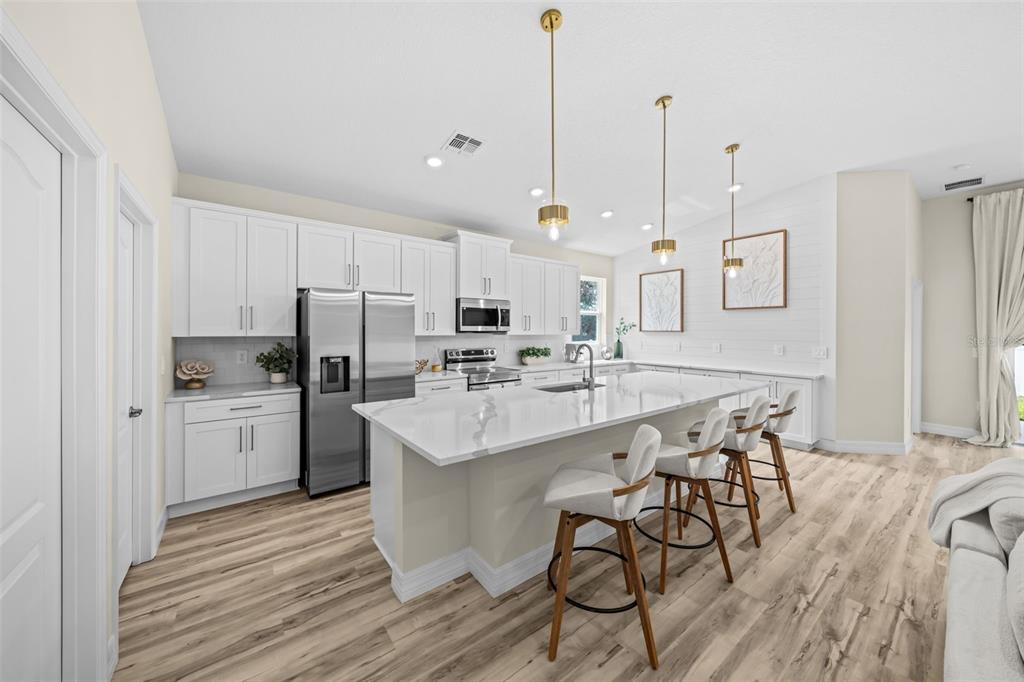 A modern kitchen features white cabinetry, a large marble-topped island, and light wood-look flooring — 3181 LA FRANCE AVENUE SW, PALM BAY, FL