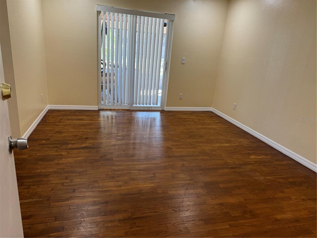 An empty room features dark wood flooring, beige walls, and a sliding glass door — 5581 AEOLUS WAY, ORLANDO, FL