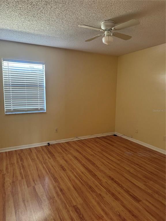 An empty bedroom features light-colored walls, wood-look flooring, a ceiling fan, and a window — 5581 AEOLUS WAY, ORLANDO, FL