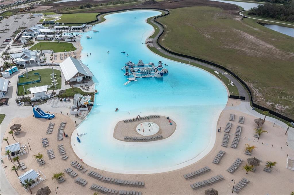 An aerial view shows a large turquoise swimming lagoon with an inflatable obstacle course — 17070 OVAL RUM DRIVE, WIMAUMA, FL