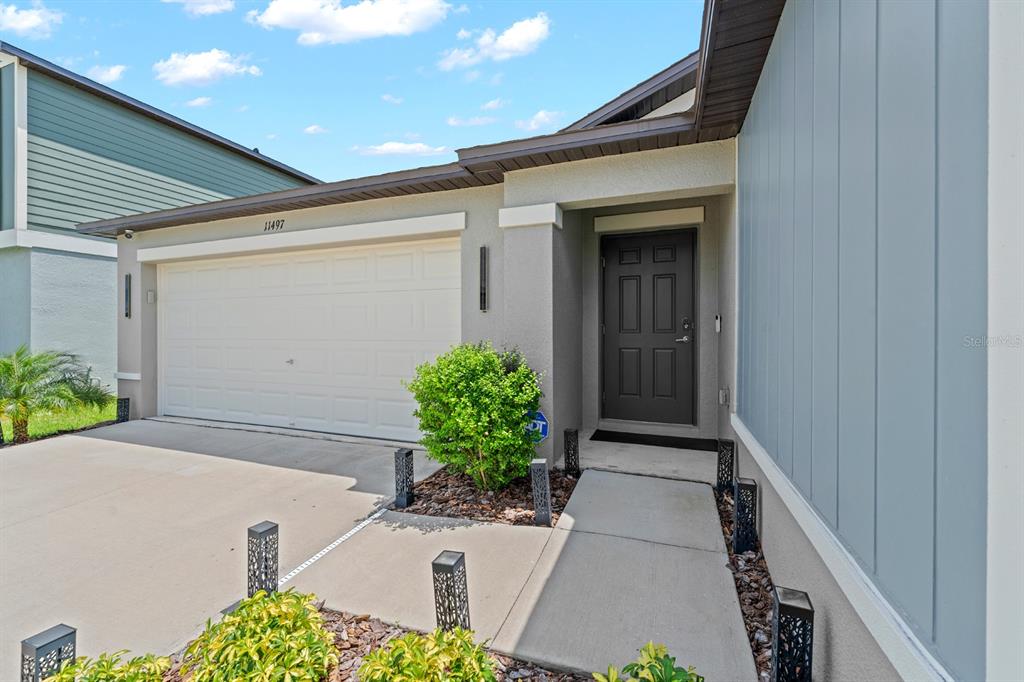 The exterior of a house features a two-car garage, a dark front door, and landscaping — 11497 LINDEN DEPOT ROAD, SAN ANTONIO, FL