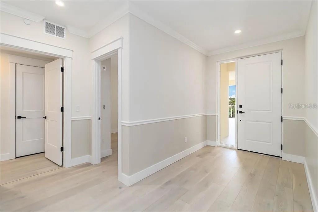 This interior entryway features light wood flooring, white walls with wainscoting, and two doorways — 280 HIDDEN BAY DRIVE UNIT 302, OSPREY, FL