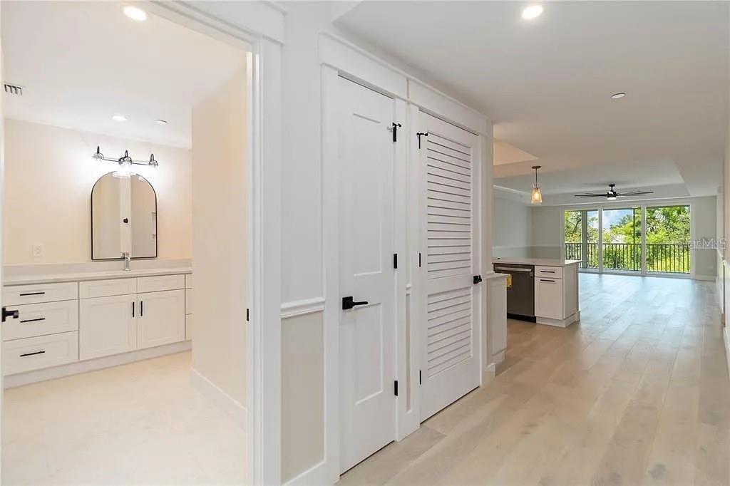 A hallway connects a white bathroom with a vanity to an open-concept kitchen and living area — 280 HIDDEN BAY DRIVE UNIT 302, OSPREY, FL