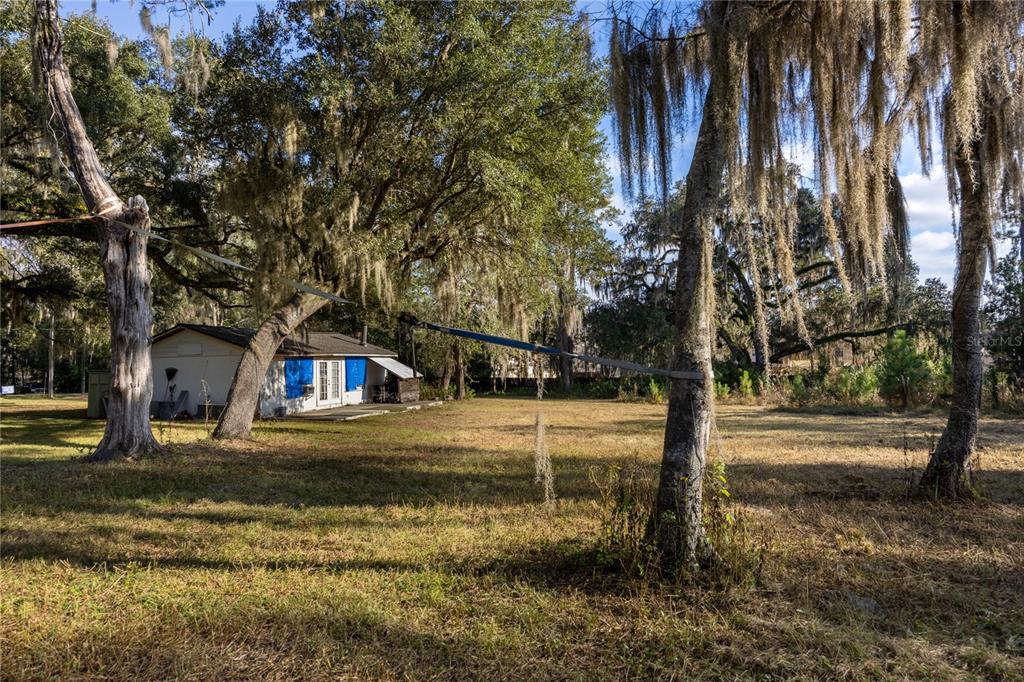 A small house with blue shutters sits on a large, grassy lot with mossy trees — 560 NW 39TH ROAD, GAINESVILLE, FL