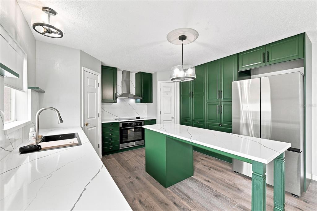 A kitchen features green cabinetry, white marble-style countertops, stainless steel appliances, and wood-look flooring — 10464 FLY FISHING STREET, RIVERVIEW, FL